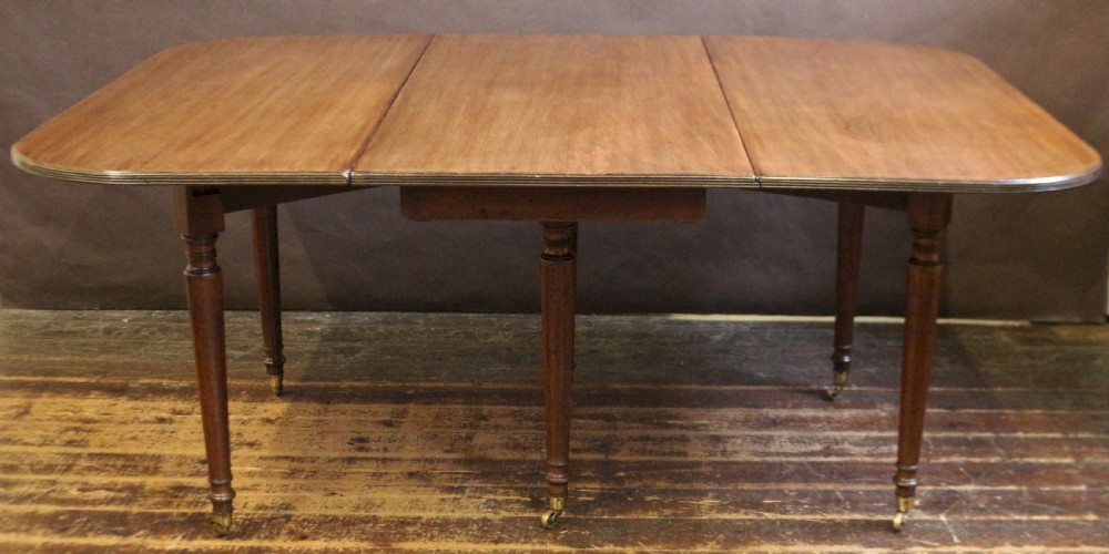 A George IV mahogany drop-leaf dining table shown with both side flaps folded down, featuring turned wooden legs and brass castors. View IV