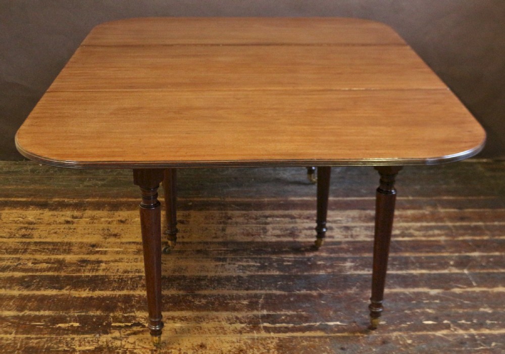 A George IV mahogany drop-leaf dining table shown with both side flaps folded down, featuring turned wooden legs and brass castors. View V