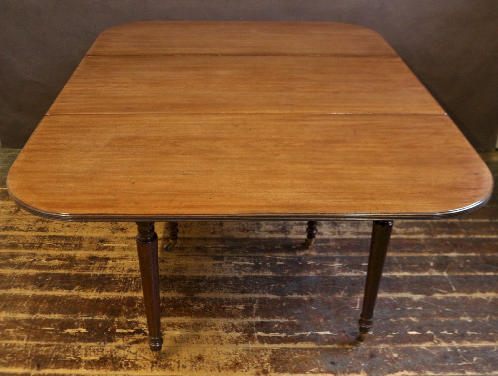A George IV mahogany drop-leaf dining table shown with both side flaps folded down, featuring turned wooden legs and brass castors. View VI