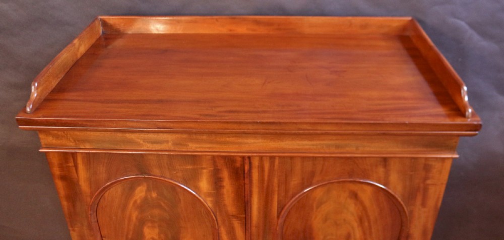 A 19th-century Victorian mahogany two-door cupboard featuring arched panel doors, rich flame veneer patterns, a low rear gallery top, and a solid plinth base. View IV