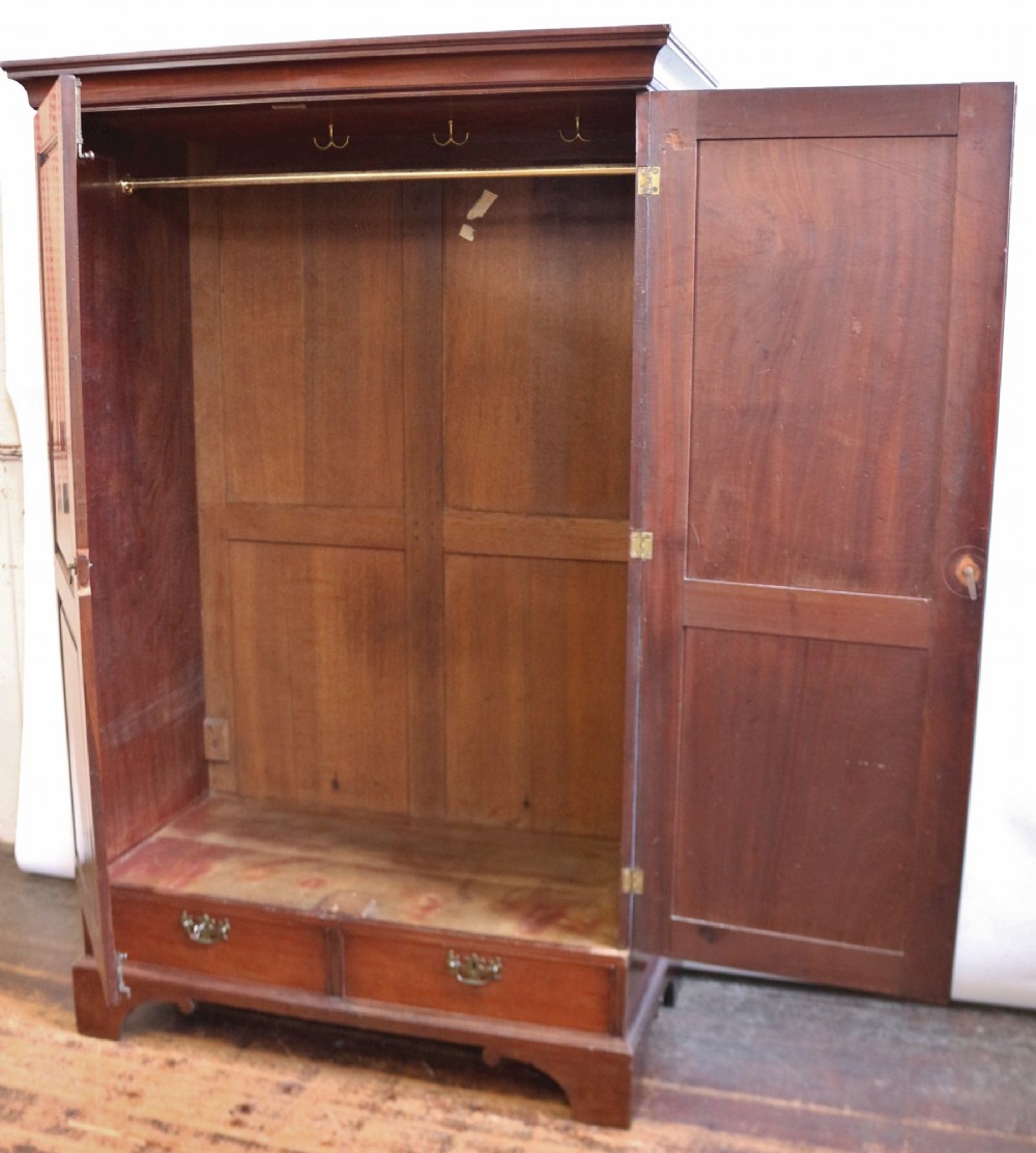 A George III mahogany two-door wardrobe featuring fielded panel doors, two base drawers with brass handles, a moulded cornice, and bracket feet. View II