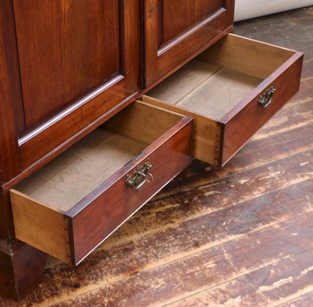 A George III mahogany two-door wardrobe featuring fielded panel doors, two base drawers with brass handles, a moulded cornice, and bracket feet. View IV