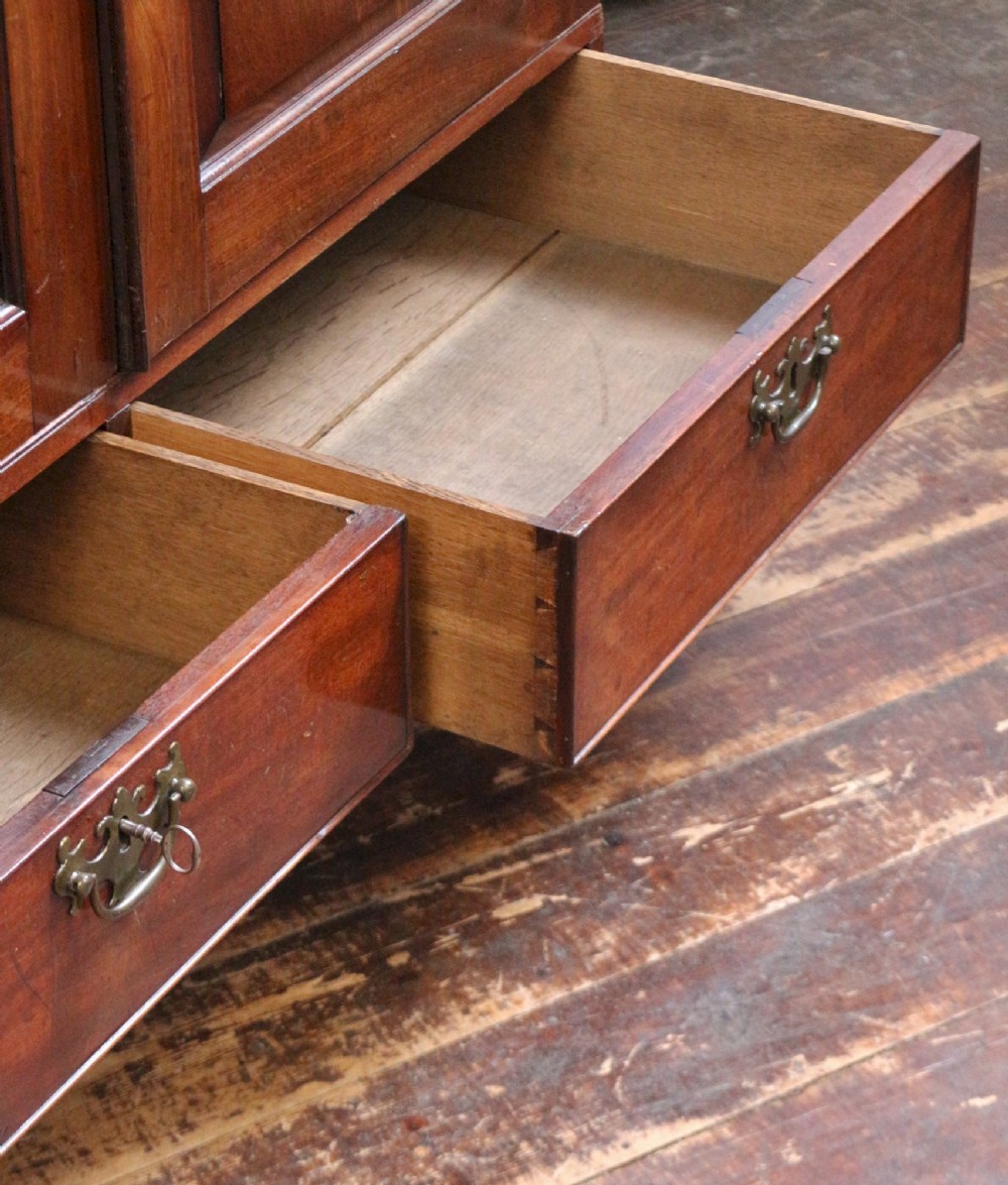 A George III mahogany two-door wardrobe featuring fielded panel doors, two base drawers with brass handles, a moulded cornice, and bracket feet. View V