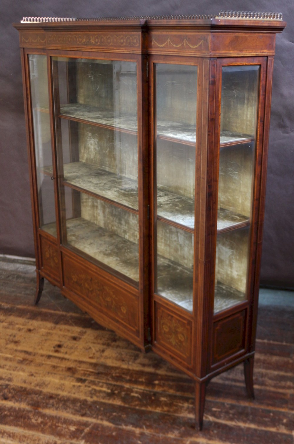 An Edwardian mahogany display cabinet featuring satinwood floral marquetry inlays, glazed doors and side panels, and square tapered legs. View V
