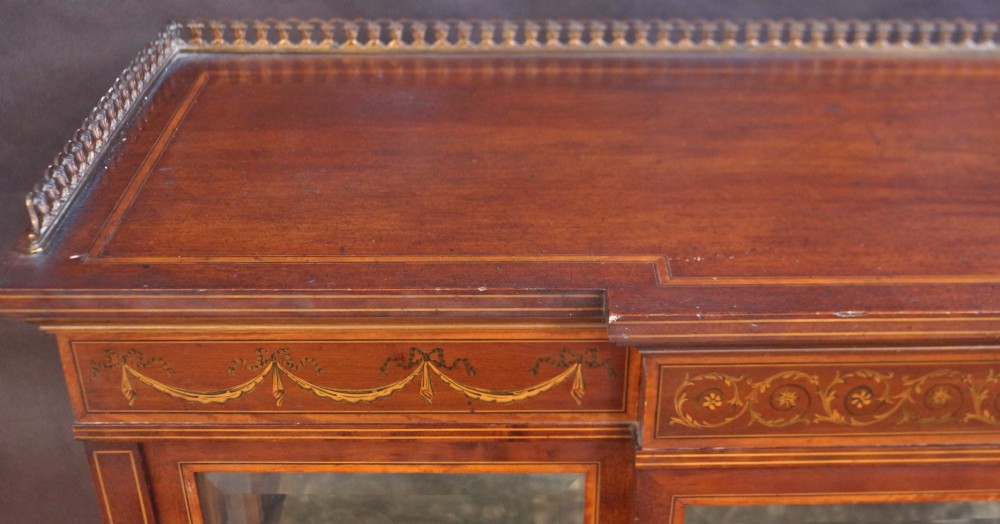 An Edwardian mahogany display cabinet featuring satinwood floral marquetry inlays, glazed doors and side panels, and square tapered legs. View VI