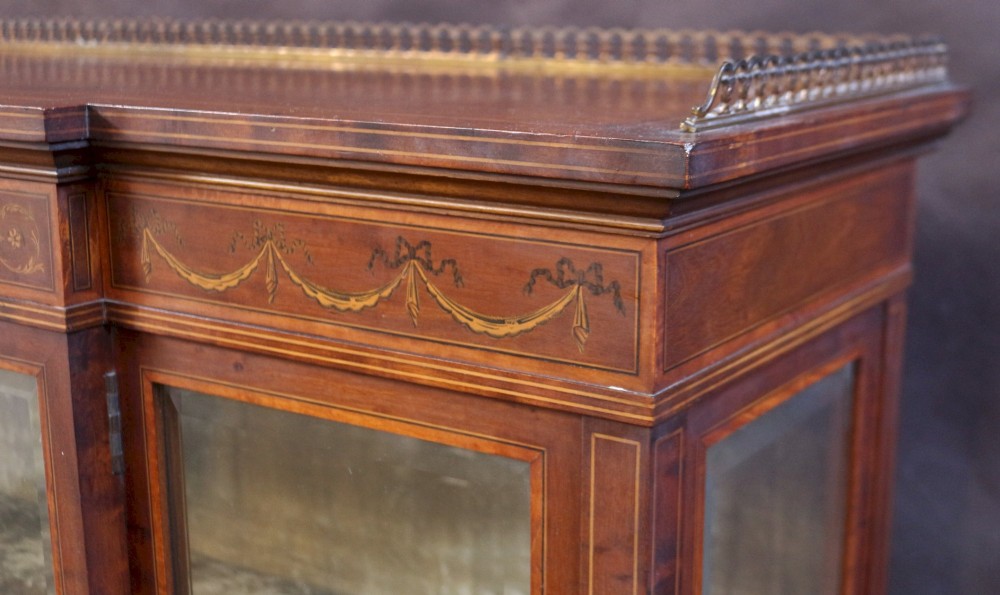 An Edwardian mahogany display cabinet featuring satinwood floral marquetry inlays, glazed doors and side panels, and square tapered legs. View IX