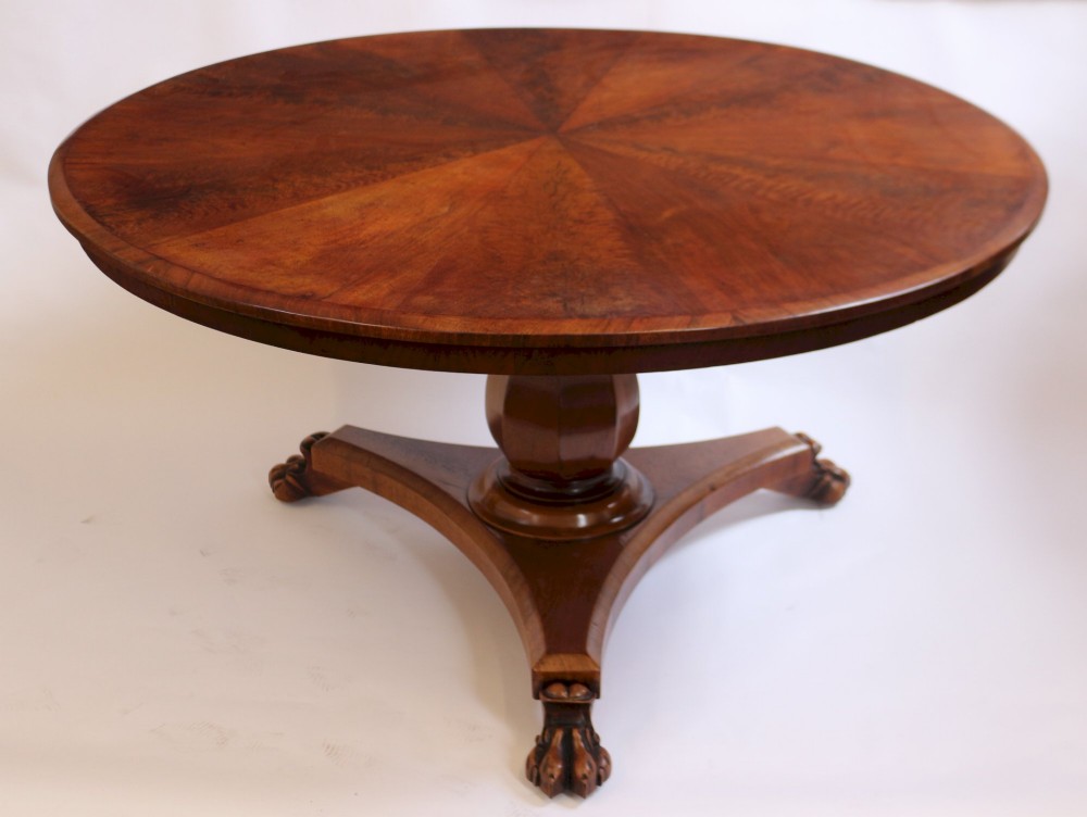 A William IV circular mahogany centre table featuring a sunburst veneered top, a central faceted column, and a triform plinth base supported by carved lion paw feet.