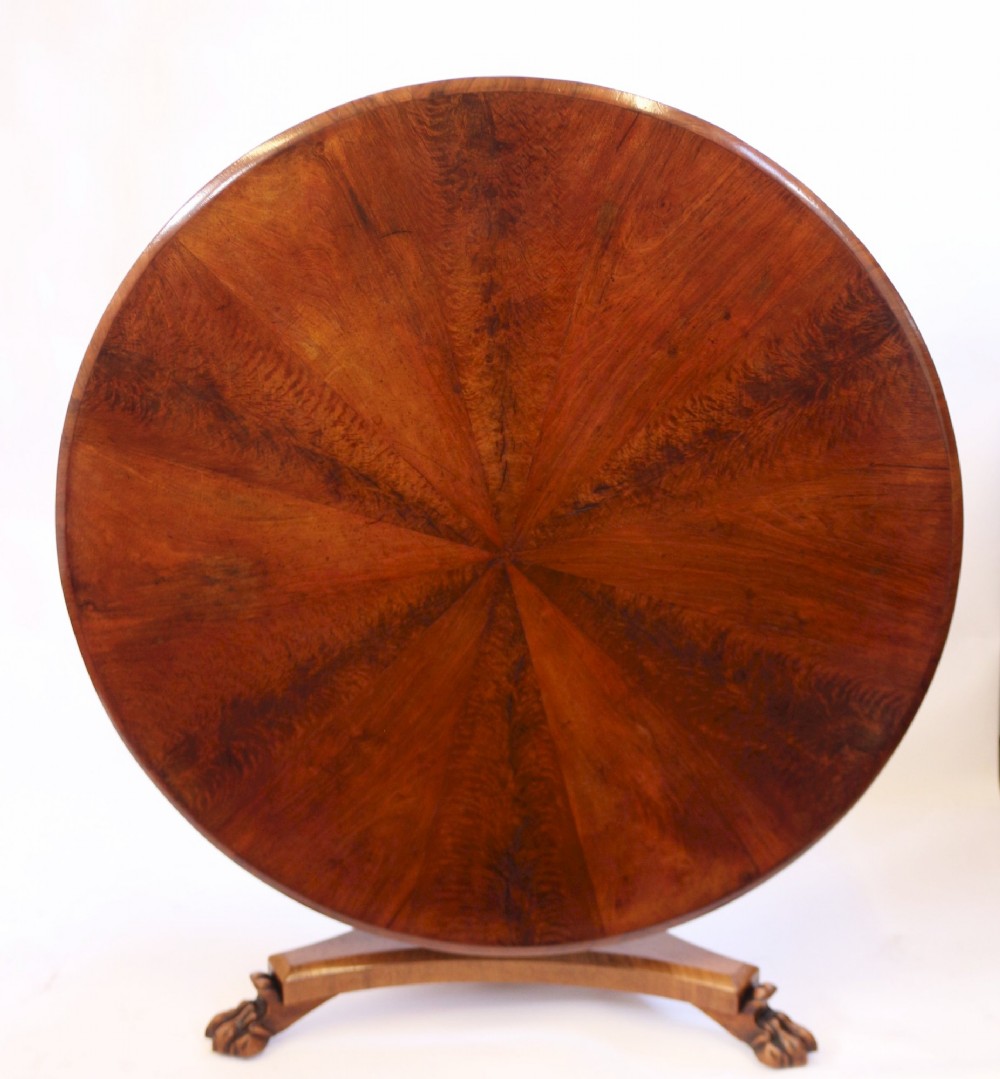 A William IV circular mahogany centre table featuring a sunburst veneered top, a central faceted column, and a triform plinth base supported by carved lion paw feet. View II