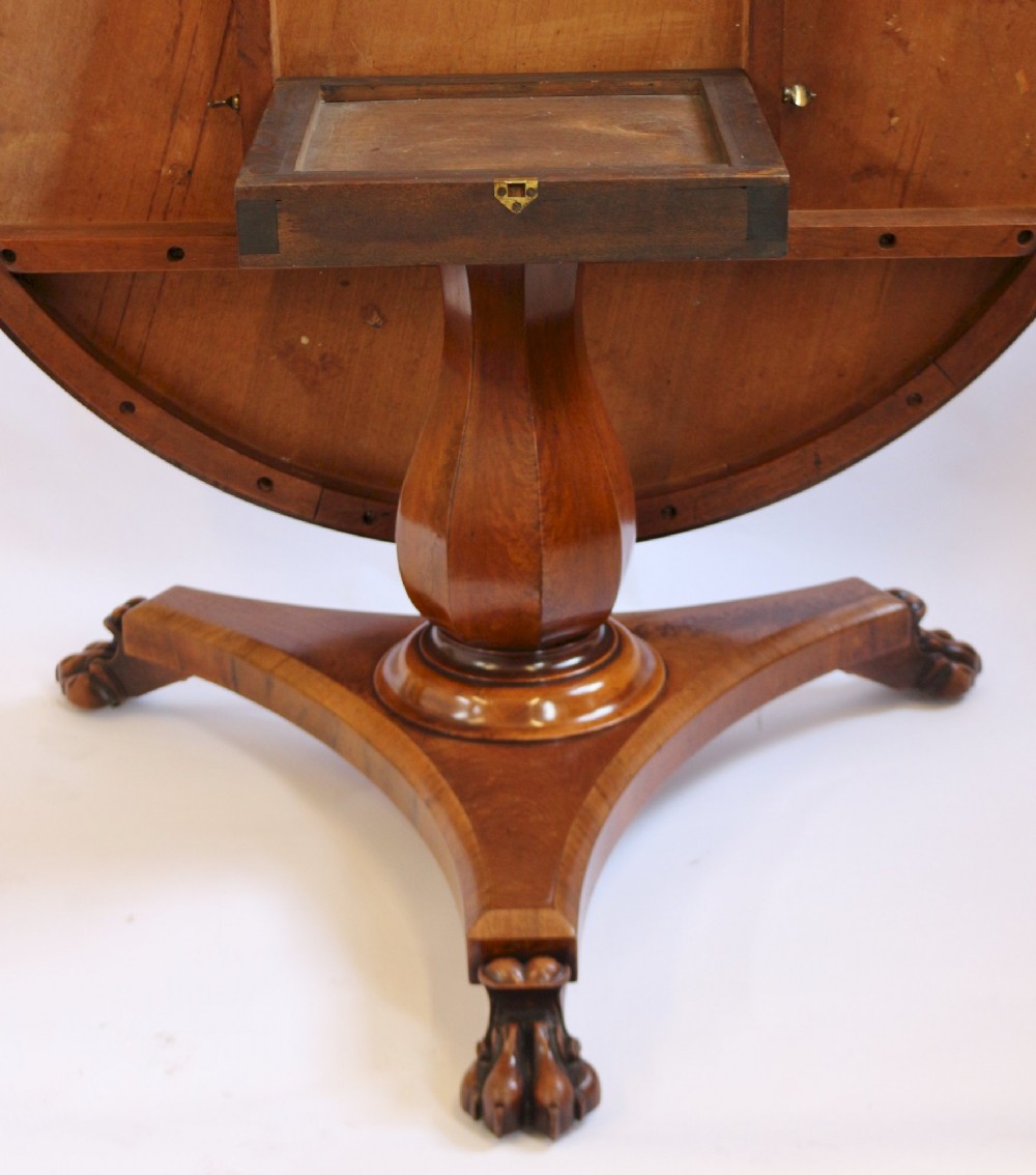 A William IV circular mahogany centre table featuring a sunburst veneered top, a central faceted column, and a triform plinth base supported by carved lion paw feet. View IV