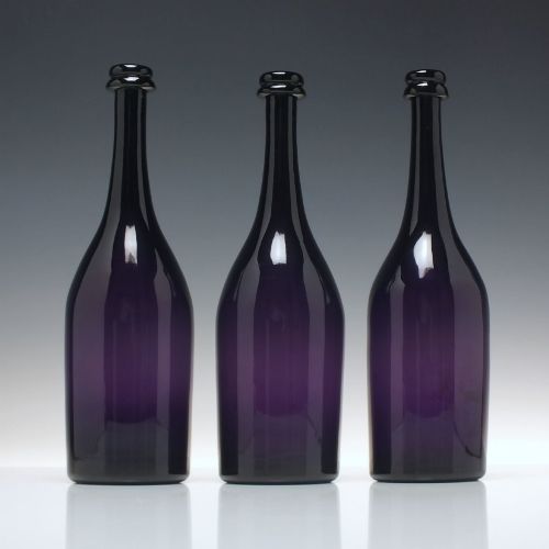 fig 1. A set of three Victorian hand-blown deep purple amethyst glass wine serving bottles featuring long tapered necks and double ring lip collars.