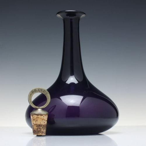 fig 3. A deep purple amethyst glass decanter featuring a wide bulbous base, elongated neck, and a metal ring stopper engraved with the word BRANDY.