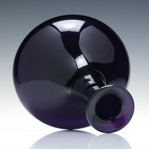 fig 4. A deep purple amethyst glass decanter featuring a wide bulbous base, elongated neck, and a metal ring stopper engraved with the word BRANDY.