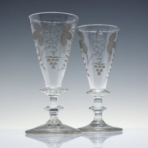 fig 1. A pair of clear hand-blown Georgian glass goblets featuring wheel-engraved motifs of hops and barley on conical bowls above knopped stems and conical bases.