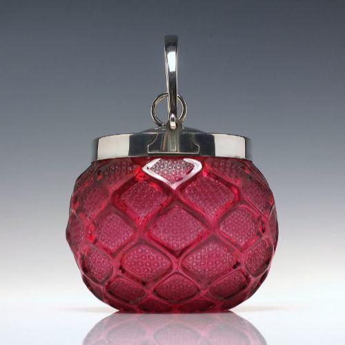 fig 1. A Victorian cranberry glass biscuit barrel featuring a diamond-quilted pattern with internal floral etching and a silver-plated rim, lid, and overhead swing handle.