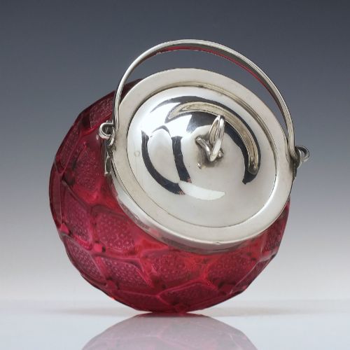 fig 2. A Victorian cranberry glass biscuit barrel featuring a diamond-quilted pattern with internal floral etching and a silver-plated rim, lid, and overhead swing handle.