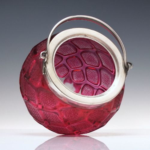 fig 3. A Victorian cranberry glass biscuit barrel featuring a diamond-quilted pattern with internal floral etching and a silver-plated rim, lid, and overhead swing handle.