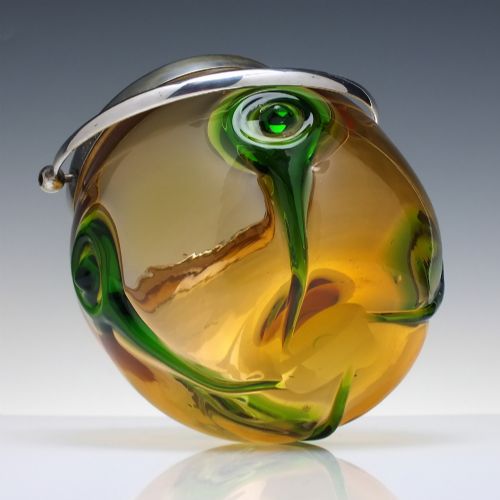 fig 4. An Art Nouveau amber glass biscuit barrel featuring green peacock eye trailing decoration and a silver-plated metal rim, lid, and swing handle.