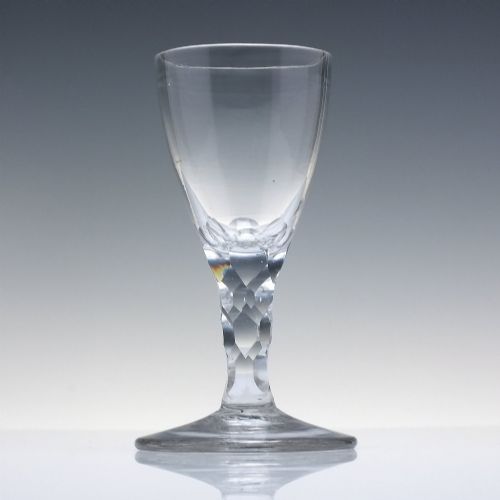 fig 1. An 18th-century clear lead crystal dram glass with a rounded bowl and a diamond facet-cut stem resting on a circular base.