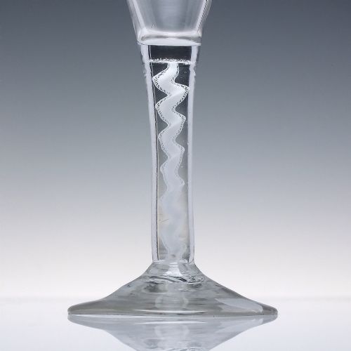 fig 2. An 18th-century clear lead glass wine glass featuring a flared trumpet bowl, a central white opaque twist stem, and a circular conical foot.