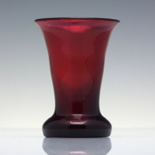 fig 1. A small Victorian ruby glass dram tumbler with a flared lip and heavy thick base against a plain background.