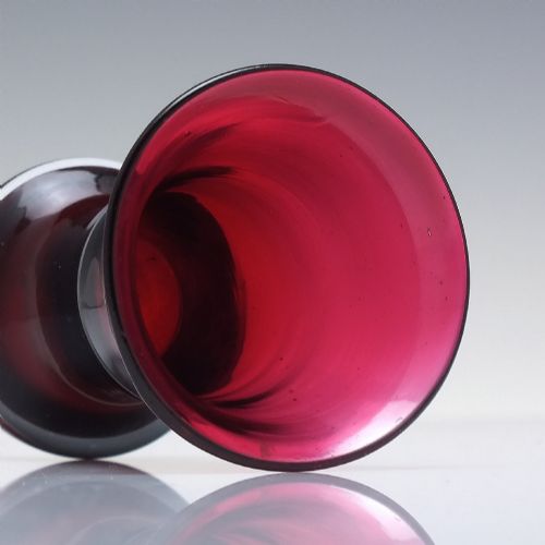 fig 2. A small Victorian ruby glass dram tumbler with a flared lip and heavy thick base against a plain background.
