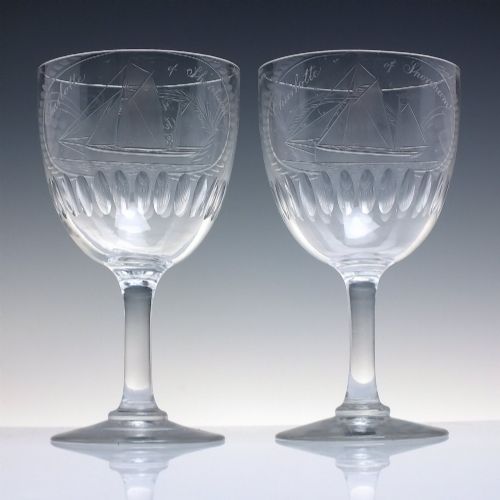 fig 1. A pair of clear glass Victorian wine goblets featuring wheel-engraved sailing ships, inscriptions, and cut oval fluting around the lower bowls.