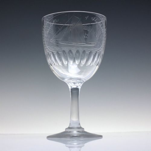 fig 2. A pair of clear glass Victorian wine goblets featuring wheel-engraved sailing ships, inscriptions, and cut oval fluting around the lower bowls.