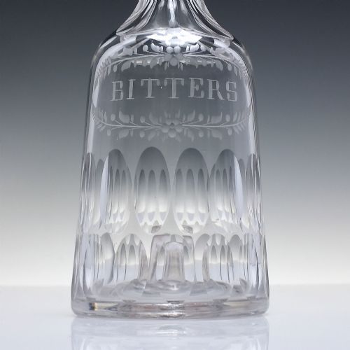 fig 3. An 18th-century clear glass sugar loaf bitters bottle featuring a faceted slender neck, cut panel base, and wheel-engraved lettering spelling BITTERS surrounded by floral swags.