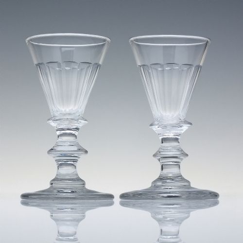 fig 1. A pair of clear cut-glass Georgian dram glasses featuring conical bowls with vertical flutes and knopped stems on circular footed bases.