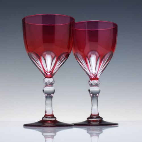 fig 1. A line of six Victorian cranberry glass wine goblets featuring cut-to-clear patterned bases and faceted clear stems.