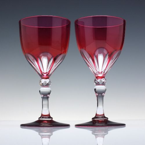 fig 2. A line of six Victorian cranberry glass wine goblets featuring cut-to-clear patterned bases and faceted clear stems.