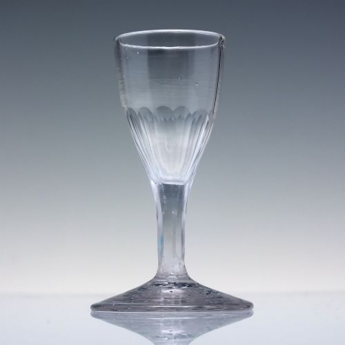 fig 1. An 18th-century clear glass tincture glass featuring a fluted lower bowl, slender stem, and wide conical foot.