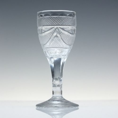 fig 1. An antique clear cut lead crystal dram glass featuring diamond lattice cutting on the bowl, a faceted stem, and a flat circular base.