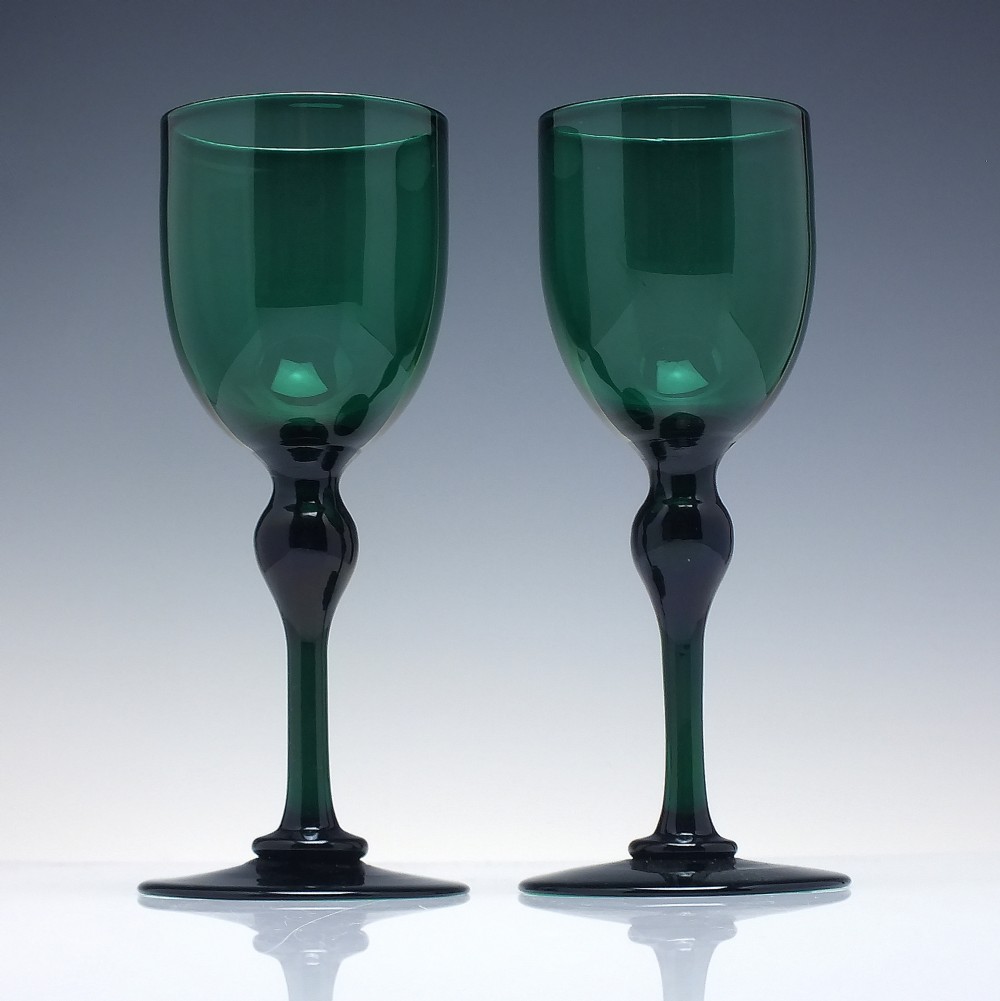 A pair of Victorian dark green hand-blown wine glasses featuring tall knopped stems and rounded bowls resting on wide circular bases.