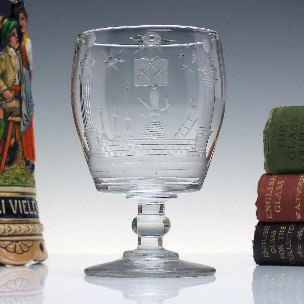 A clear 19th-century glass rummer featuring detailed wheel-engraved Masonic symbols, a knopped stem, and a flat circular base.