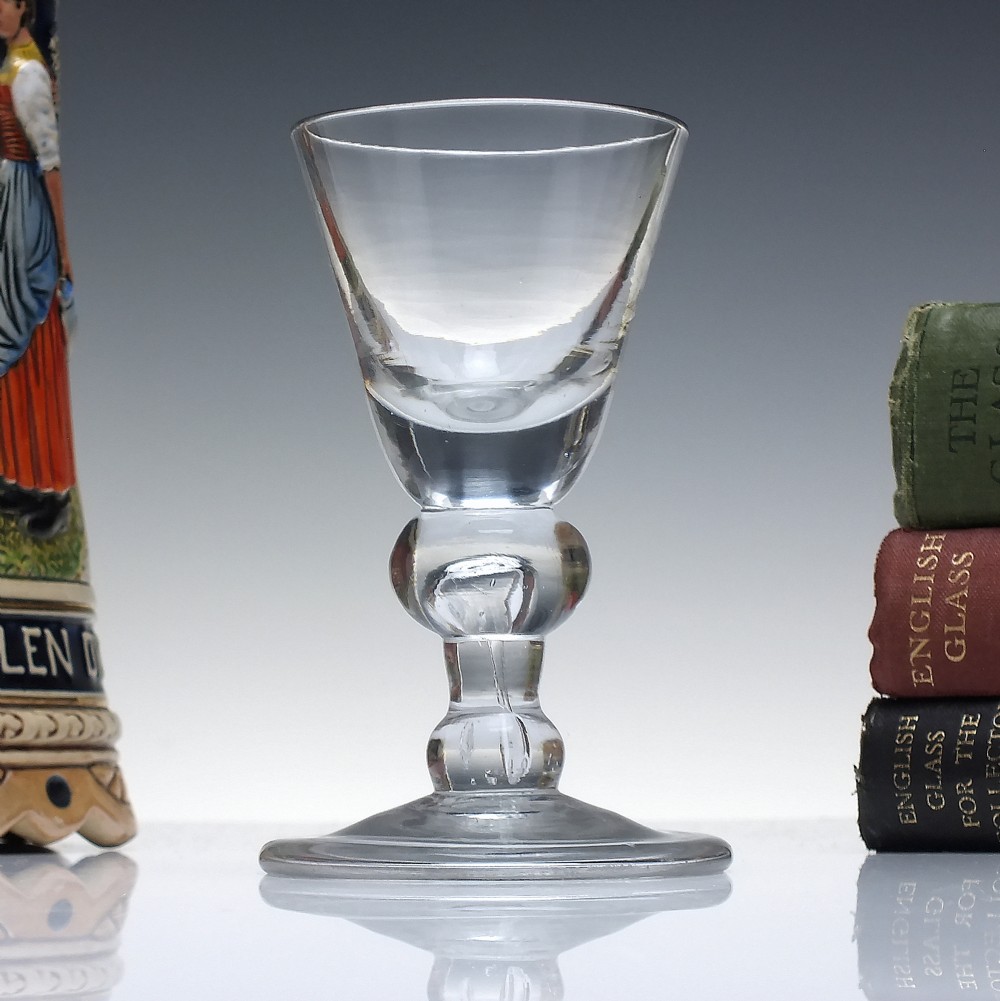 An early 18th-century clear lead glass dram vessel featuring a trumpet-shaped bowl and a heavy baluster knopped stem on a circular foot.