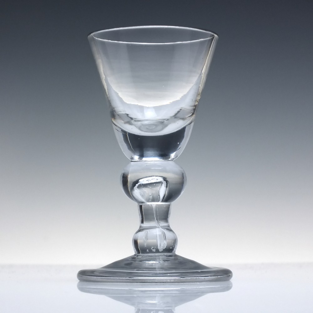 An early 18th-century clear lead glass dram vessel featuring a trumpet-shaped bowl and a heavy baluster knopped stem on a circular foot. View II