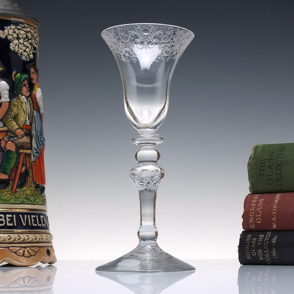 An 18th-century clear glass wine goblet featuring a wheel-engraved Rococo rim, a light baluster stem with knops, and a conical foot.