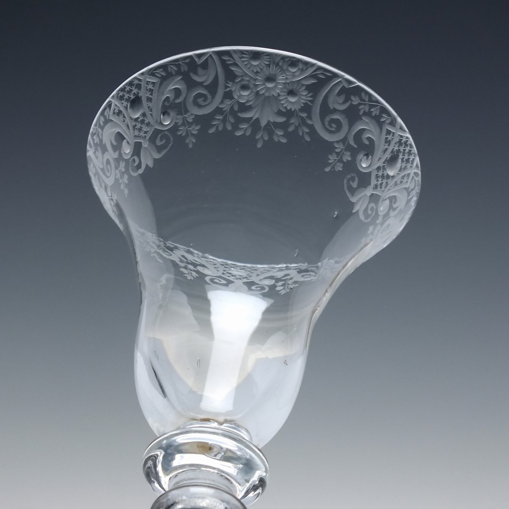 An 18th-century clear glass wine goblet featuring a wheel-engraved Rococo rim, a light baluster stem with knops, and a conical foot. View V