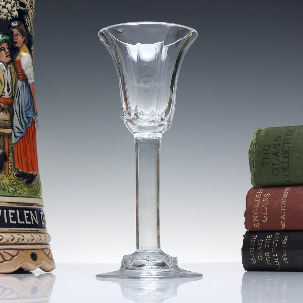 An 18th-century clear lead glass wine goblet featuring an inverted petal moulded bowl, a tall plain stem, and a circular foot.