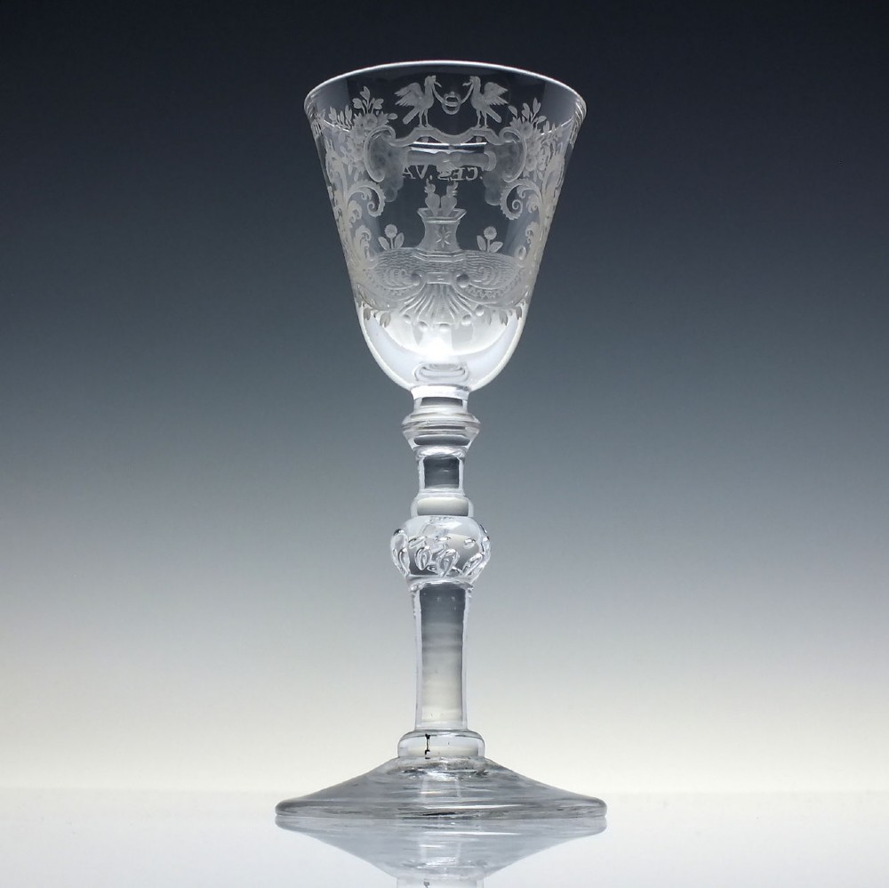 An 18th-century clear lead glass wine goblet featuring detailed wheel-engraved marriage motifs on the bowl and a knopped light baluster stem.