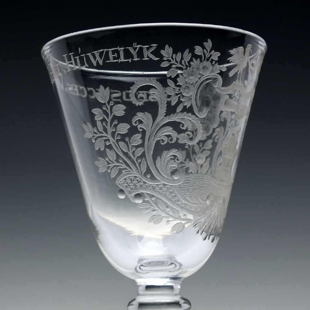 An 18th-century clear lead glass wine goblet featuring detailed wheel-engraved marriage motifs on the bowl and a knopped light baluster stem. View V