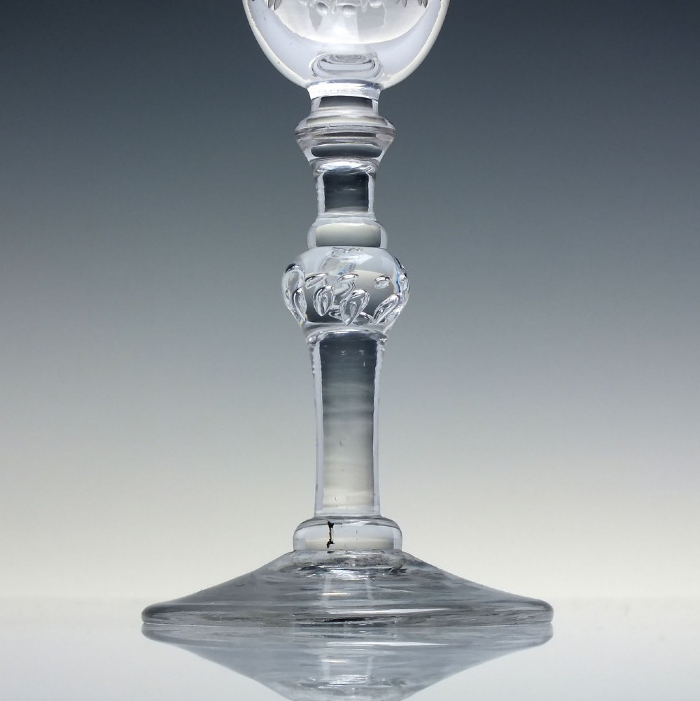 An 18th-century clear lead glass wine goblet featuring detailed wheel-engraved marriage motifs on the bowl and a knopped light baluster stem. View VIII