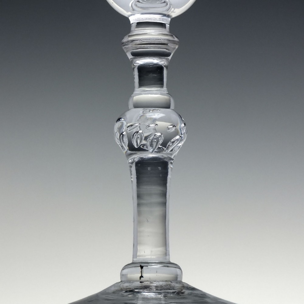 An 18th-century clear lead glass wine goblet featuring detailed wheel-engraved marriage motifs on the bowl and a knopped light baluster stem. View IX
