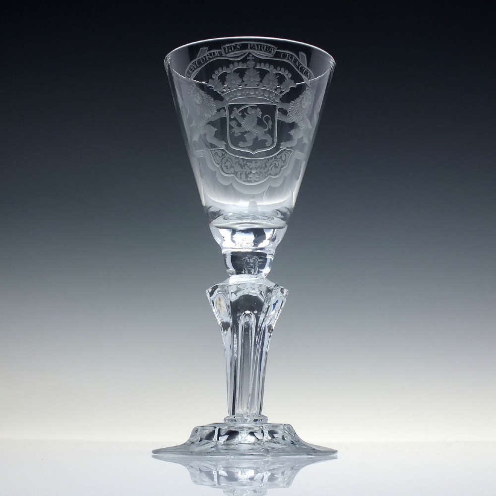 An 18th-century clear glass wine goblet with a wheel-engraved heraldic coat of arms on the bowl, a moulded pedestal stem, and a flat circular foot.