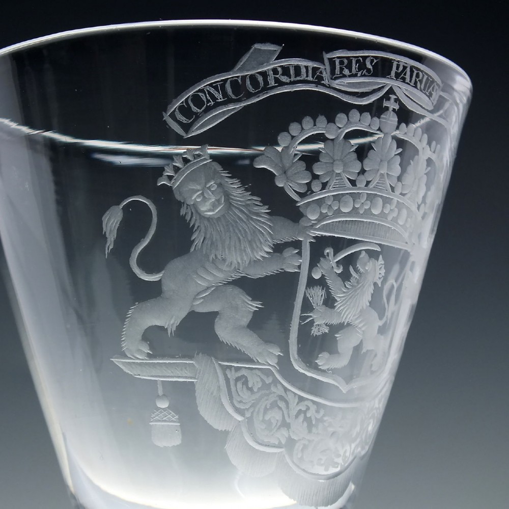 An 18th-century clear glass wine goblet with a wheel-engraved heraldic coat of arms on the bowl, a moulded pedestal stem, and a flat circular foot. View V