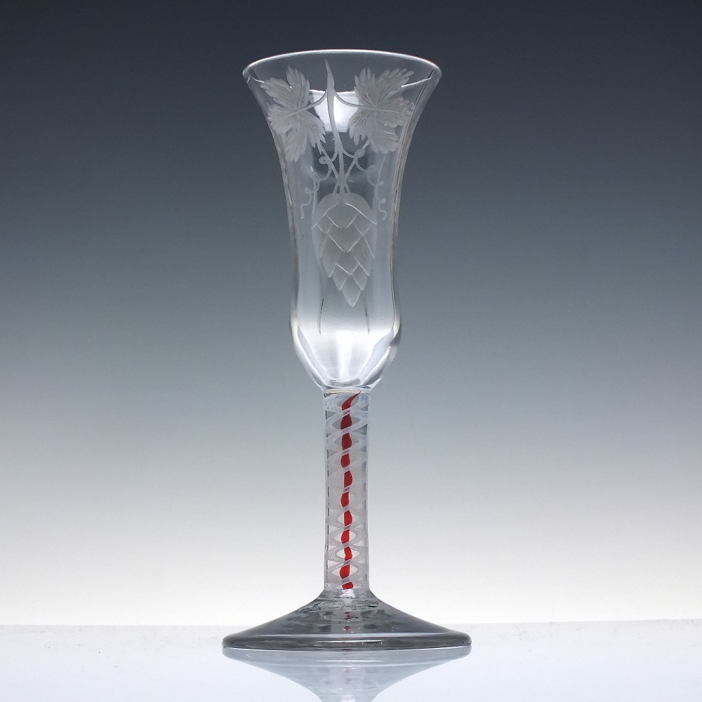 An eighteenth-century clear lead glass ale flute featuring a flared rim, floral hop wheel engravings, and a central stem containing a red and opaque white spiral twist. View II