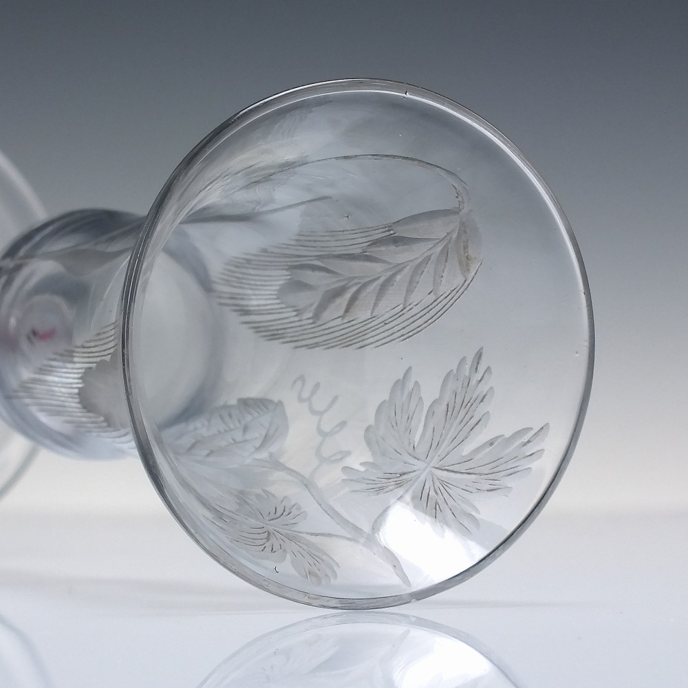 An eighteenth-century clear lead glass ale flute featuring a flared rim, floral hop wheel engravings, and a central stem containing a red and opaque white spiral twist. View VII