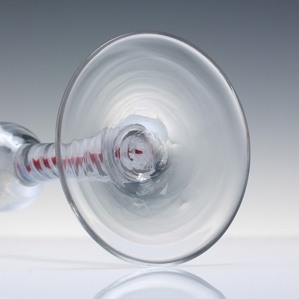 An eighteenth-century clear lead glass ale flute featuring a flared rim, floral hop wheel engravings, and a central stem containing a red and opaque white spiral twist. View VIII