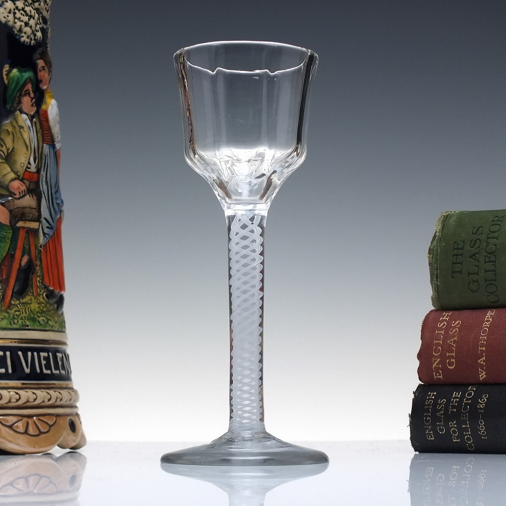An 18th-century clear glass wine vessel featuring a ribbed ogee bowl supported by a stem with an internal white opaque twist motif resting on a conical foot.